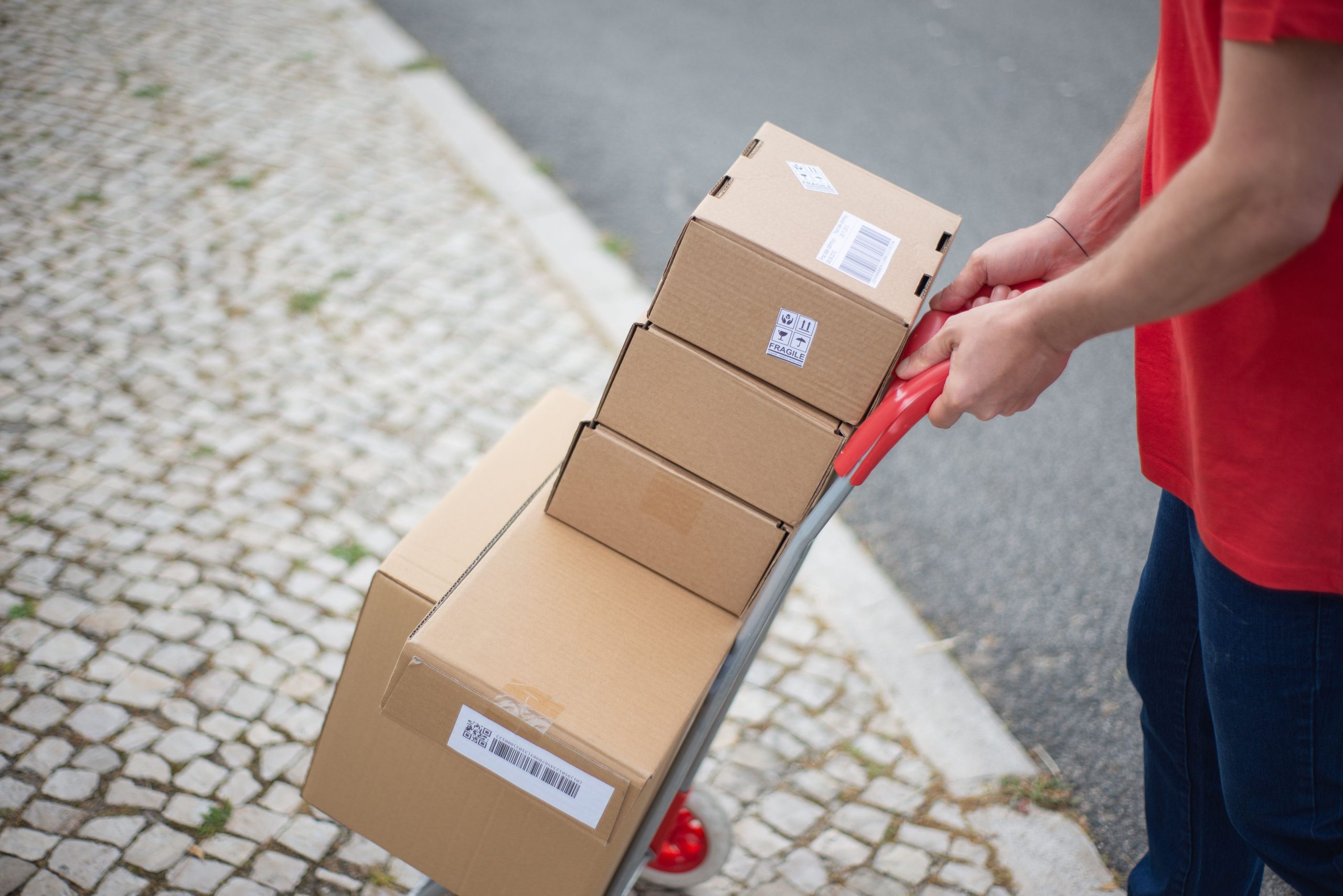 Courier handling packages with a cart on a cobblestone street in daylight.